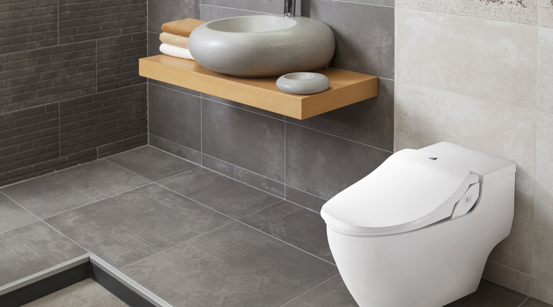 A Slim Two bidet seat installed on a low, tankless toilet in a gray-tiled bathroom.