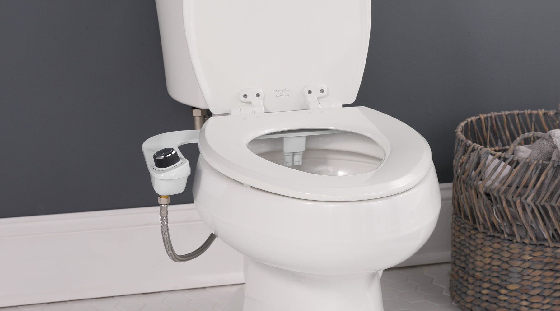 Close-up of a toilet with a Slim Edge bidet attachment installed. The attachment has a black knob.