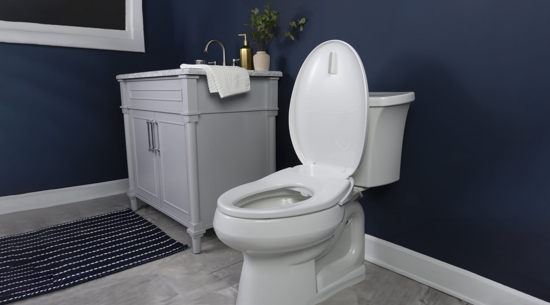 A toilet with a BB-500 toilet seat installed. It's in a dark blue bathroom, next to a white sink.